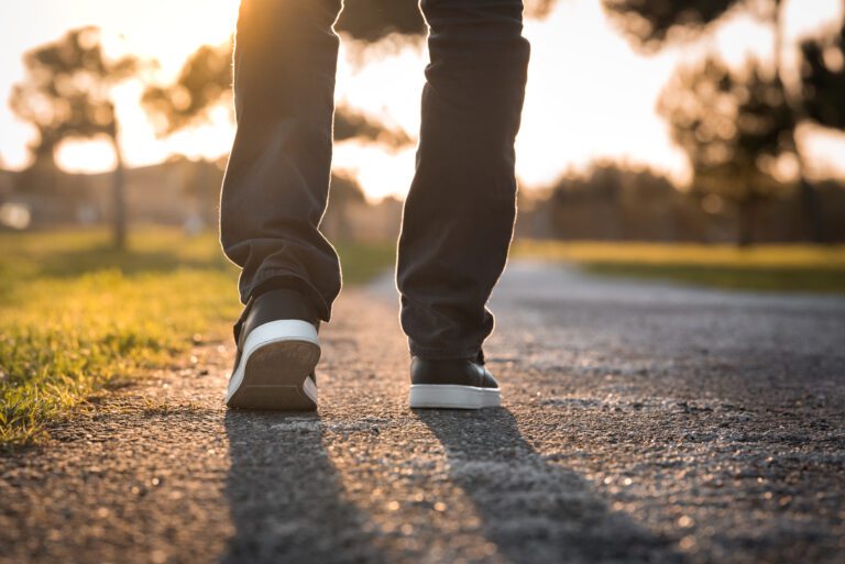 Man walking outdoors in the park at sunset. Closeup on shoe, taking a step